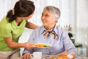 Caregiver bringing food to happy senior woman