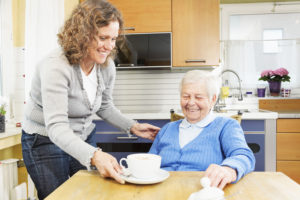 Family caregiver handing cup of coffee to happy senior woman