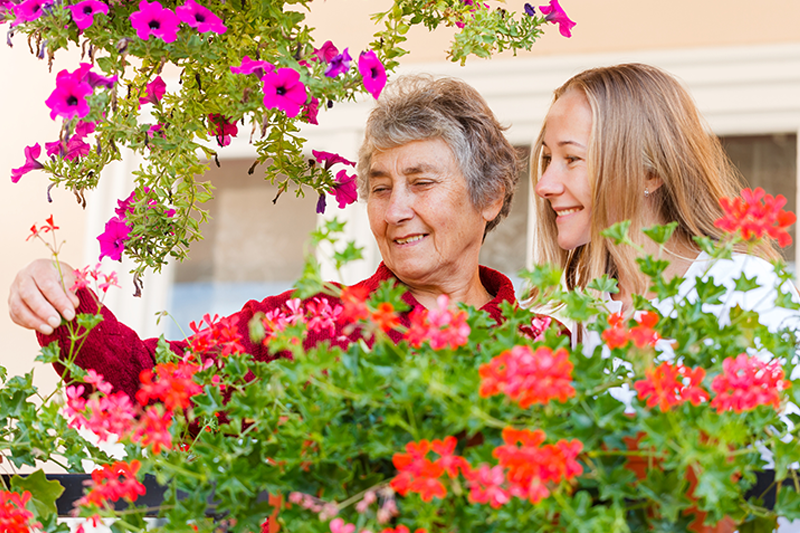 Senior woman with alzheimers looking at flowers with caregiver
