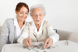 A woman engages in dementia-friendly activities, such as putting together a puzzle, with her elderly mother.